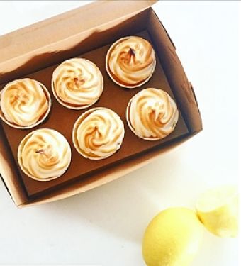 A box, with six Lemon Meringue Cupcakes, surrounded by Lemons